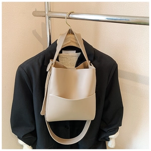 Sac seau en cuir beige avec surpiqûres blanches contrastées sur fond de blazer noir