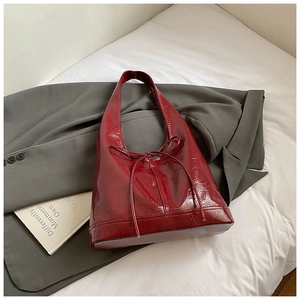Detailed view of the glossy wine red patent leather shoulder bag with a bow accent