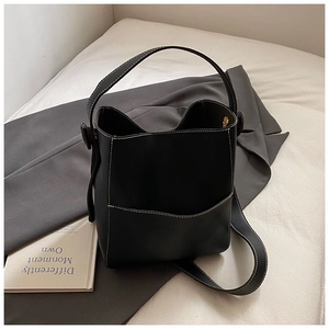 Détail du sac seau noir avec surpiqûres blanches contrastées et poche avant sur décor épuré