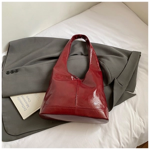 Deep red patent leather tote bag with vintage texture placed on a grey blazer