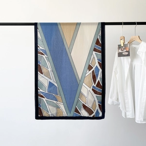 Detail of herringbone silk scarf with blue and beige geometric patterns hanging on a rack