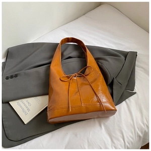 Close-up of caramel glossy tote bag with bow detail on a grey suit jacket