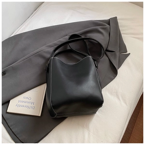 Gros plan d'un sac seau noir avec surpiqûres blanches sur fond de costume gris