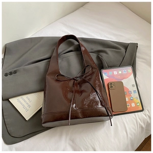 Detail of dark brown glossy patent leather tote bag with elegant bow accent and large capacity