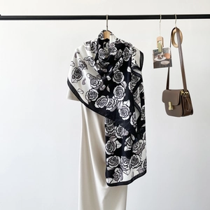 Detailed shot of a black and white rose pattern long silk scarf styled on a white dress