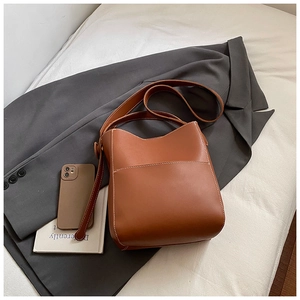 Gros plan du sac seau en cuir marron avec surpiqûres blanches et poche frontale