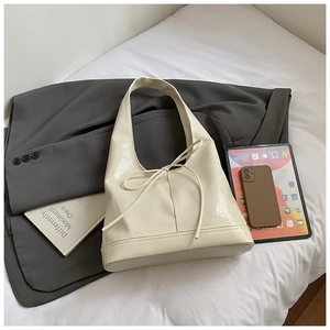 Detailed view of cream-white faux leather tote bag with bow detail in a lifestyle setting