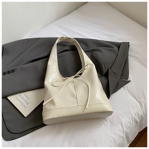 Detail view of cream oversized tote bag with bow tie accent on a grey suit background
