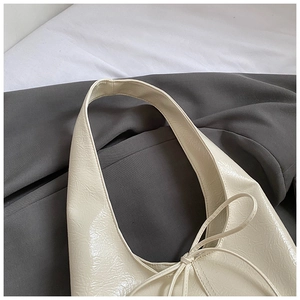 Detailed close-up of cream bow shoulder bag with glossy wrinkled faux leather texture