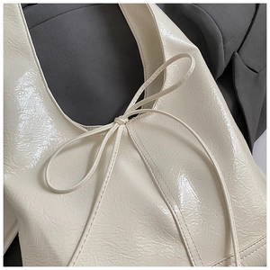 Close-up of cream white glossy tote bag featuring unique pleated texture and bow detail