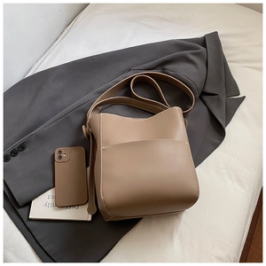 Détails d'un sac seau en cuir kaki avec surpiqûres blanches sur un fond de blazer gris