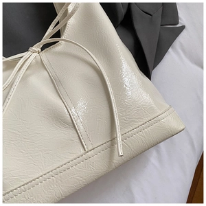 Close-up of cream white glossy patent leather tote bag with stylish bow tie detail