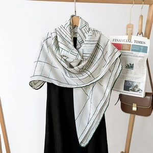 Detail of white scarf with green geometric pattern draped on a black dress with wood hanger
