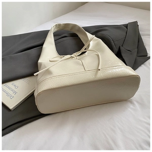 Detail of a creamy white tote bag featuring glossy crinkled leather and a bow decoration