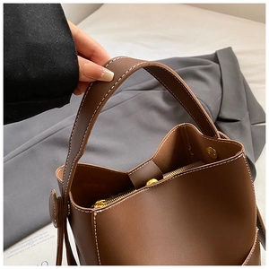 Gros plan sur un sac seau en cuir marron avec surpiqûres blanches et zip doré luxueux