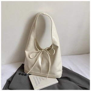 Detail of a creamy white tote bag featuring glossy patent leather and a ribbon bow