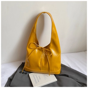 Detail shot of bright yellow glossy leather tote bag with elegant bow and textured finish