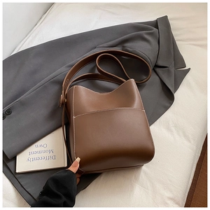 Détail du sac seau en cuir marron avec surpiqûres blanches et poche frontale