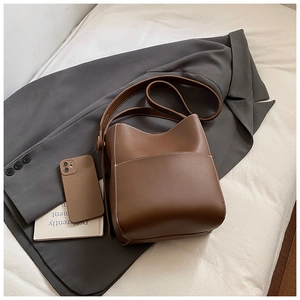 Détail du sac seau en cuir marron avec surpiqûres blanches sur un blazer gris chic