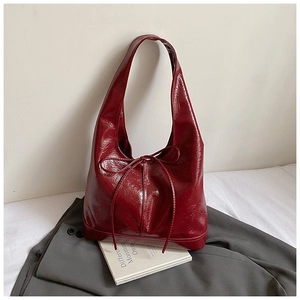 Detail of burgundy glossy leather hobo bag with a delicate bow strap on a minimal background