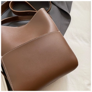 Gros plan détaillé du sac seau en cuir marron avec coutures blanches et bandoulière large