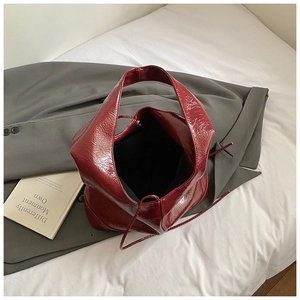 Close-up of dark red patent leather tote bag with crinkled texture and sleek inner lining