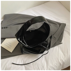 Glossy black bow-style bucket bag with pleated texture on a premium grey blazer background