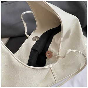 Detailed close-up of cream pleated tote bag with silver magnetic closure and black lining
