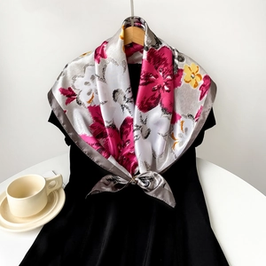 Detail of silk satin scarf with floral pattern tied to a dress using a golden clip