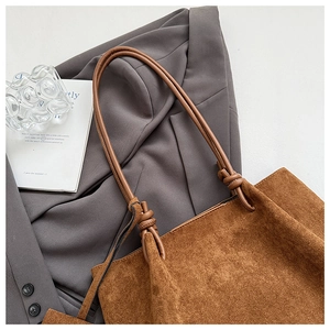 Detail of brown matte tote bag with knotted shoulder strap on grey blazer background