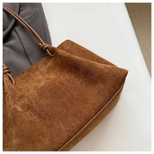 Detail of a brown suede tote bag featuring a decorative knot design on the shoulder strap