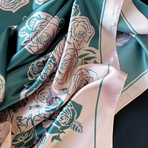 Dettaglio di elegante foulard in raso verde scuro con stampe di rose e finitura lucida