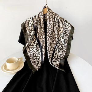 Detail of satin floral scarf draped on hanger showing silky texture and olive green border
