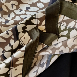 Detail of satin scarf fabric showing abstract floral pattern and fine machine-hemmed edges