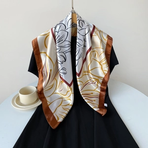 Detail of a 90cm square satin silk scarf with elegant gold floral prints and brown borders