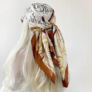 Detail of silk-satin square scarf with floral print and orange borders worn as headscarf