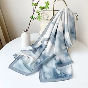 Détail d'une écharpe paysage gris-bleu drapée sur un sac à main en cuir beige