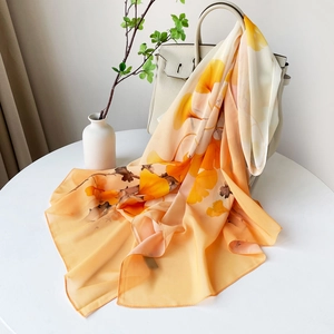 Détail d'une écharpe à imprimé ginkgo orange drapée sur un sac à main en cuir blanc