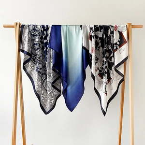 Close-up of three elegant silk scarves with paisley and floral prints on wooden hangers