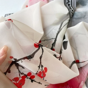 Gros plan montrant la texture translucide et l'imprimé de fleurs de prunier du foulard en soie
