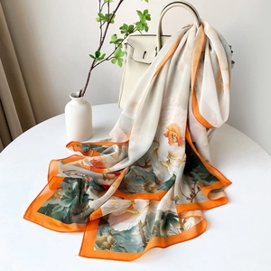Vue détaillée d'une écharpe en soie à fleurs avec bordures oranges sur table blanche
