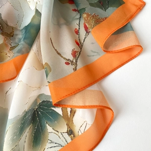 Détail rapproché d'une écharpe en satin floral soyeux avec des bordures orange vif