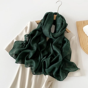 Detalle de bufanda de seda verde oscuro con textura de rejilla sobre un vestido