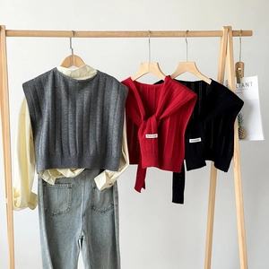 Detailed knit texture of solid color shawls in grey, red, and black hanging on wooden racks