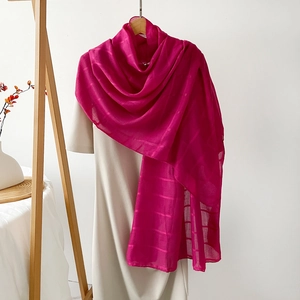 Detalle de una bufanda larga de color rojo rosa con patrón de cuadros sobre un vestido