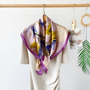 Detail view of abstract printed satin silk scarf styled as an accessory on a cream dress