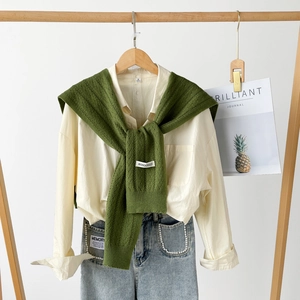 Detailed view of a green knitted shawl over a white shirt with elegant pearl denim accents