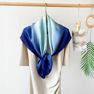 Detail of blue gradient silk satin scarf draped on a minimalist wooden hanger
