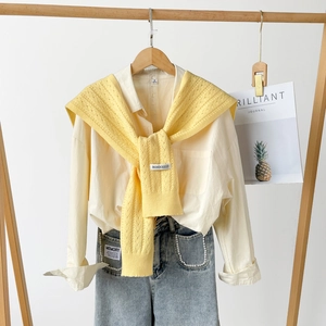 Detail of yellow hollow knit shawl with BONOGEED label over a cream collared shirt