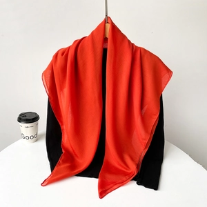 Detail of vibrant red sheer chiffon headscarf draped over a black knit top stylishly